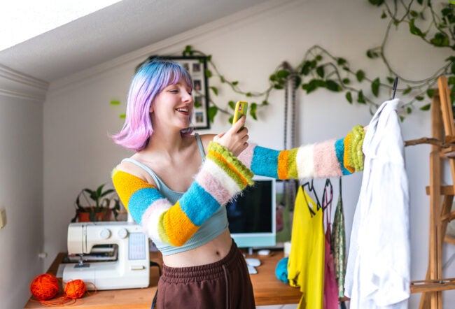 A young fashionable person takes a picture of a shirt with their phone, showing the rise of retailers reselling items to cater to Gen Z consumers
