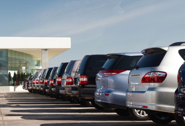 A row of parked cars in front of a modern building, likely a car dealership.