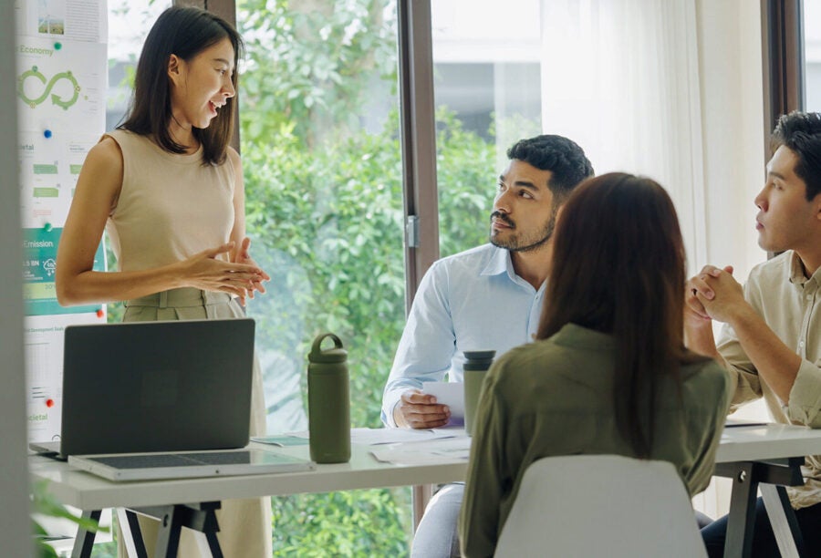 Employee standing in front of ESG-related diagrams and presenting to her colleagues at a meeting table