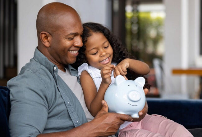 Father and daughter sitting on the couch with a piggy bank